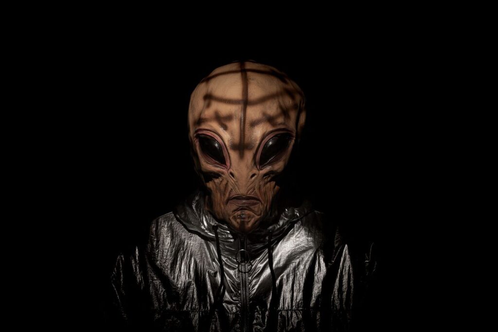 Why aliens are (probably) too lazy to make first contact Anthropomorphic alien creature in futuristic silver spacesuit looking at camera at dark night.