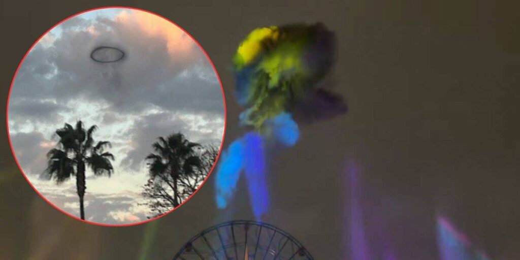 A dark ring-shaped cloud floating above palm trees and a ferris wheel in a cloudy sky, with colorful lights beaming upward.