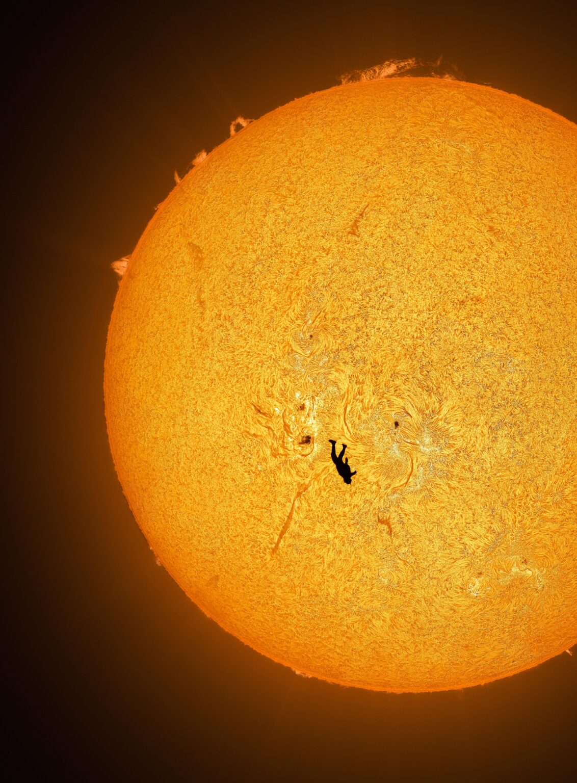 I captured my friend in freefall while skydiving with a hydrogen alpha telescope, revealing the details of the solar atmosphere behind his silhouette. [OC]