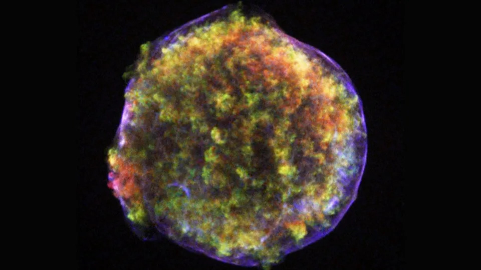  A cloud of orange and yellow gas inside a ring of purple shows the remnant of a supernova explosion in deep space. 