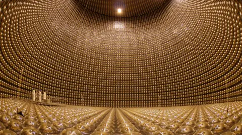 Kamioka/ICRR/Tokyo University A giant room filled with gold colouted globes forming the floor and the curved walls. In the background three scientists can be made out dwarfed by the scale of the complex