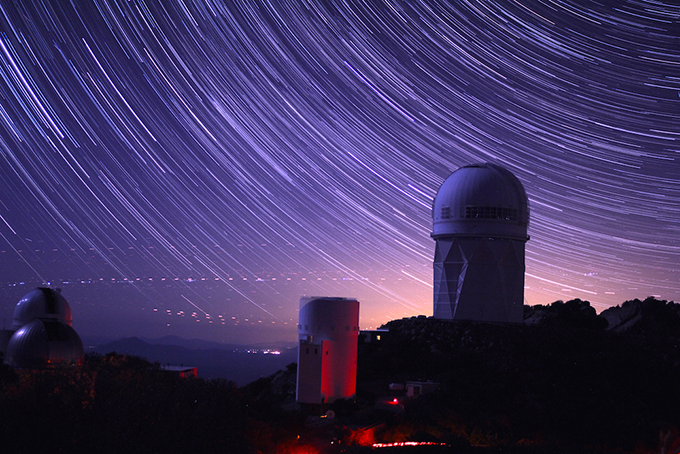 an extended release photo of the DESI telescope tower at night, stars streaking across the sky above it