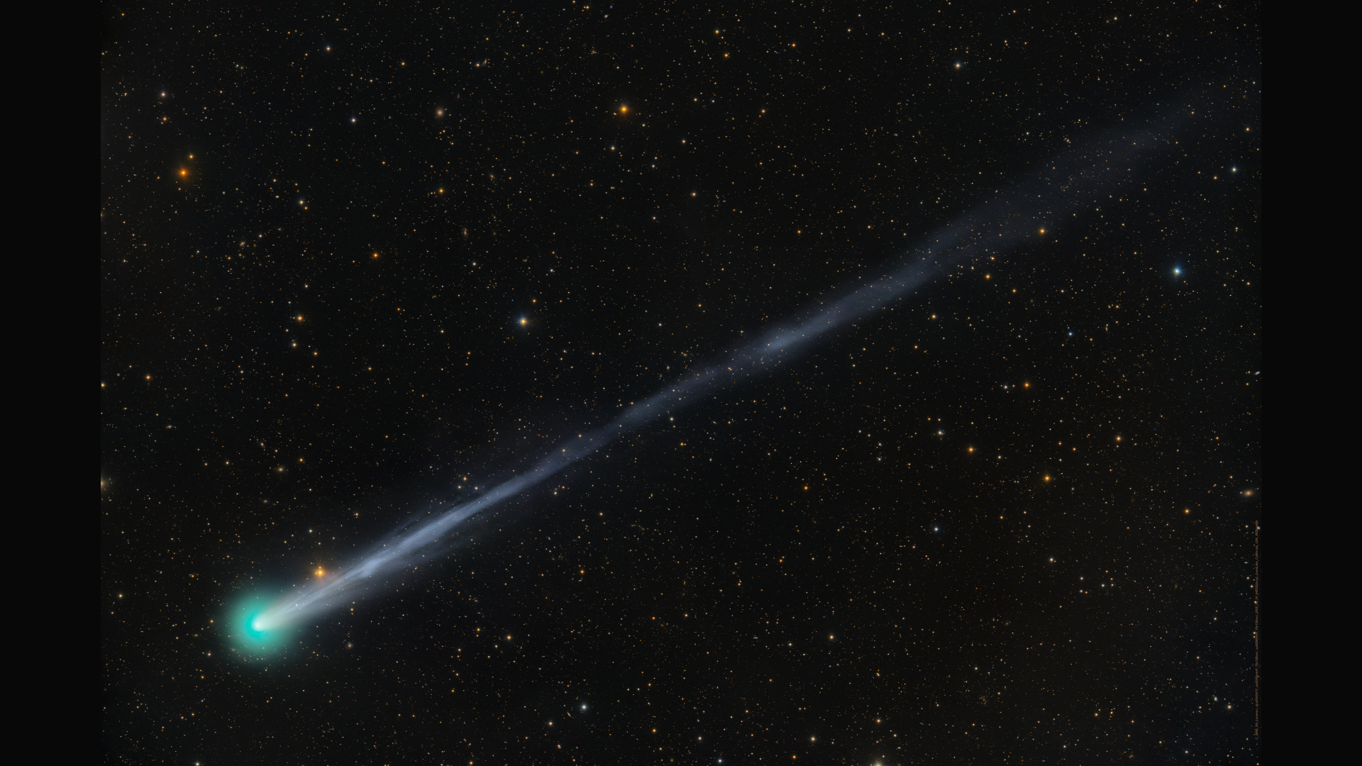 A bright green comet is pictured to the bottom left of a starfield against a black sky, with a long tail extending to the upper right of the screen.