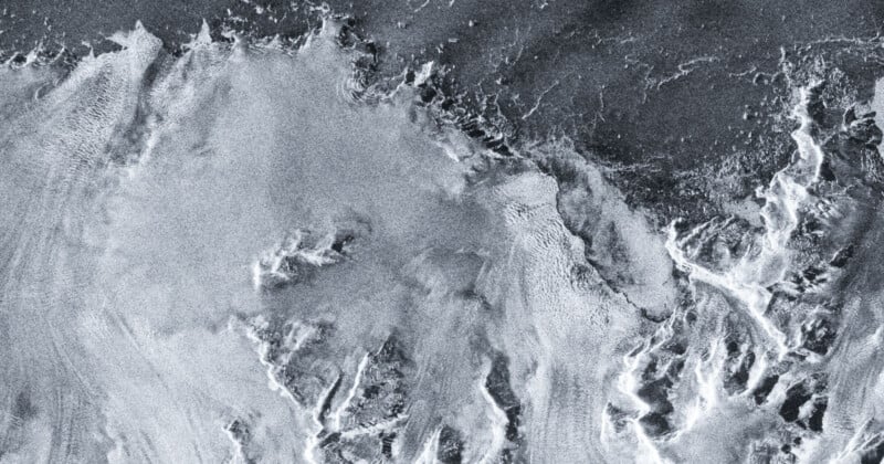 A grayscale aerial image shows swirling patterns resembling ice, snow, or frothy water with contrasting light and dark areas, creating an abstract, textured landscape.
