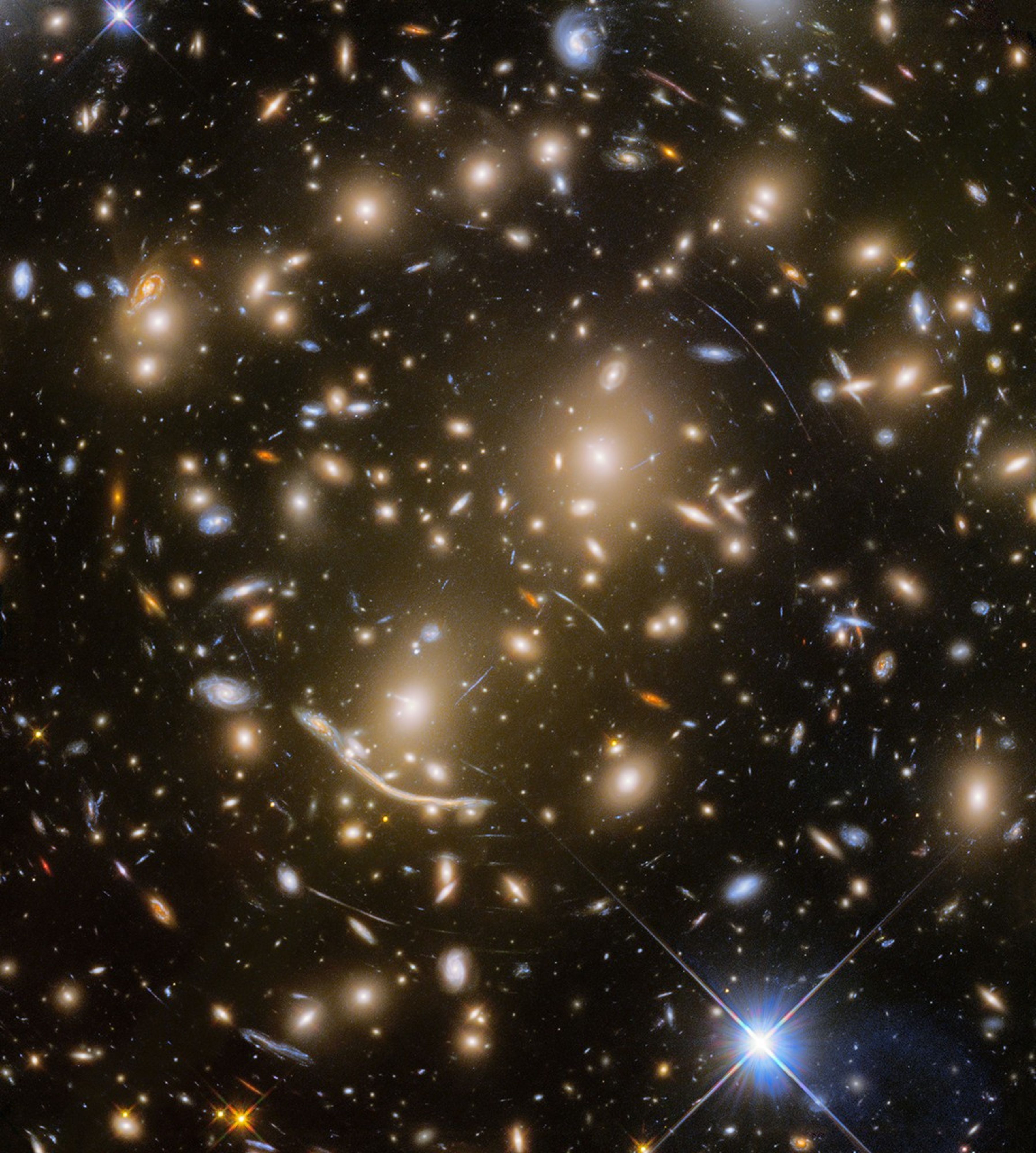 A field of galaxies along with the curved arcs of gravitationally lensed galaxies.