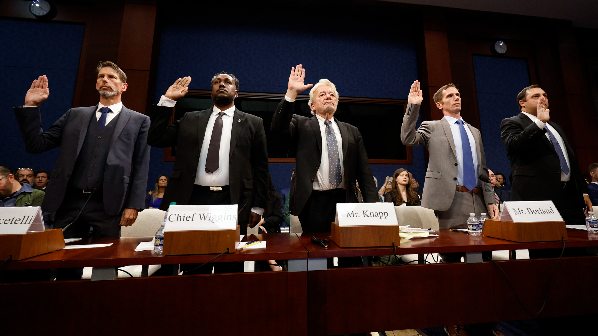 Five men wearing suits and ties raise their right hands behind a table to begin the Congressional hearing