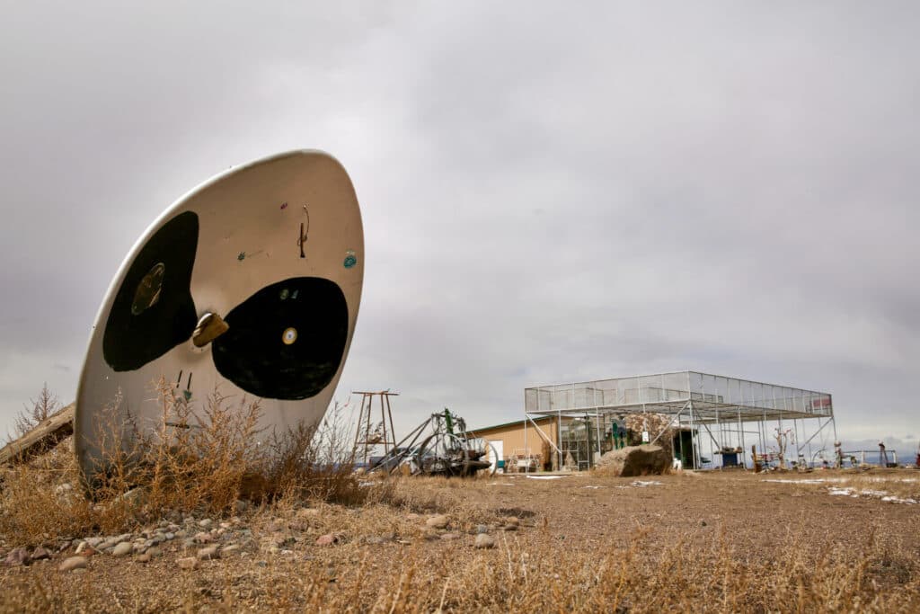 A satellite dish is painted white with black eyes. The UFO Watchtower tourist attraction is seen in the background.