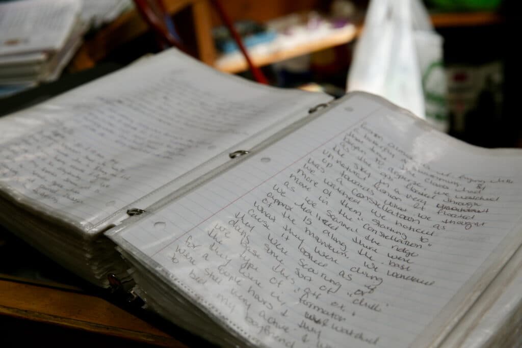 A three-ring binder with handwritten pages is featured prominently in the frame.