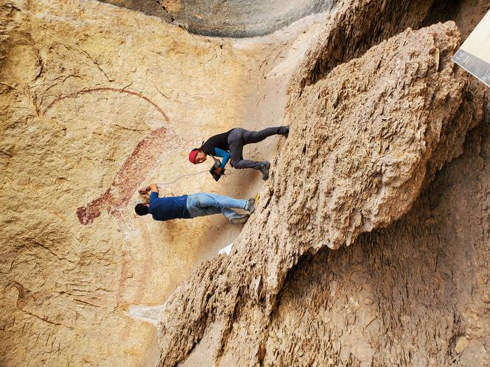 A man and a woman hover over some rock paintings on the side of a cliff.