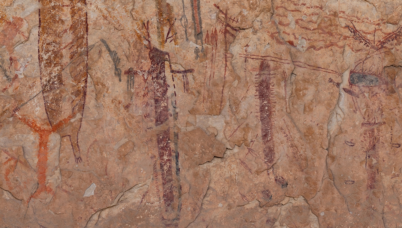 Rock art with red paint. we see vertical figures on a wall.