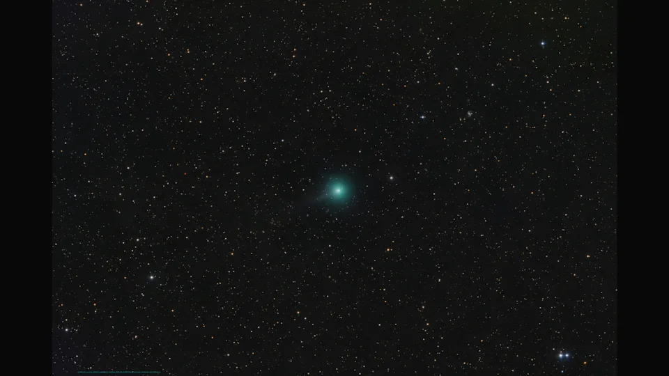 A bright green comet is pictured to the bottom left of a starfield against a black sky, with a long tail extending to the upper right of the screen.