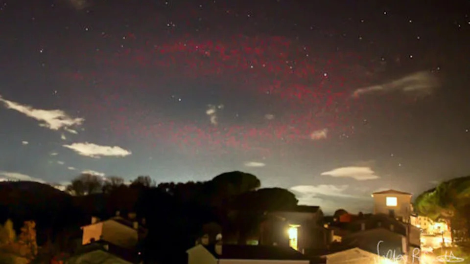  A photograph of a blurry red ring of light in the night sky above a town in Italy. 