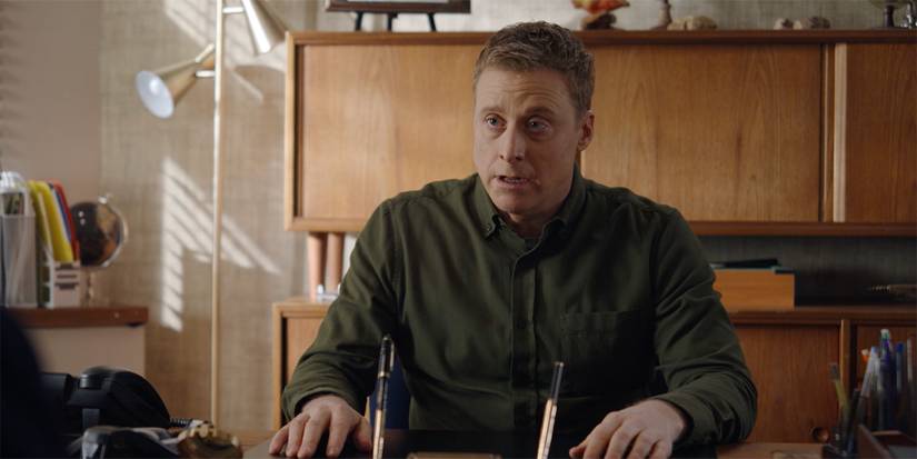 Alan Tudyk as Harry sitting behind his desk in Resident Alien.