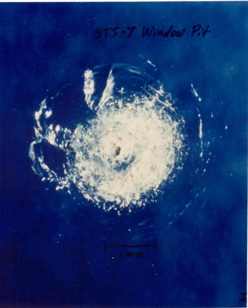 An impact crater on one of the windows of the Space Shuttle Challenger following a collision with a paint chip during STS-7.