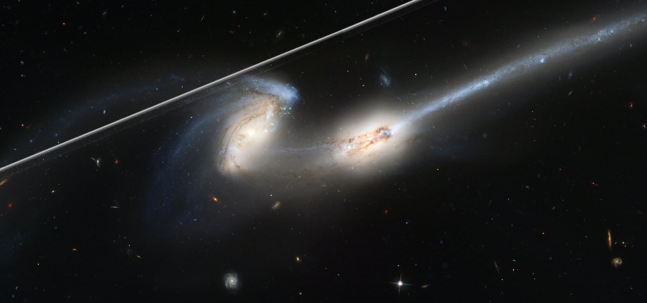 An image of two interacting galaxies with a streak of light in the upper left.