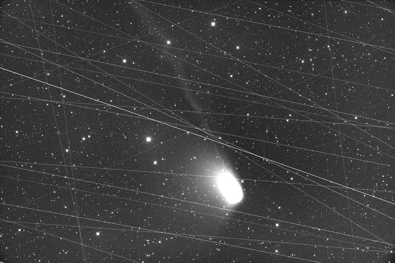 A photo of a fuzzy comet with more than a dozen streaks of light through it.