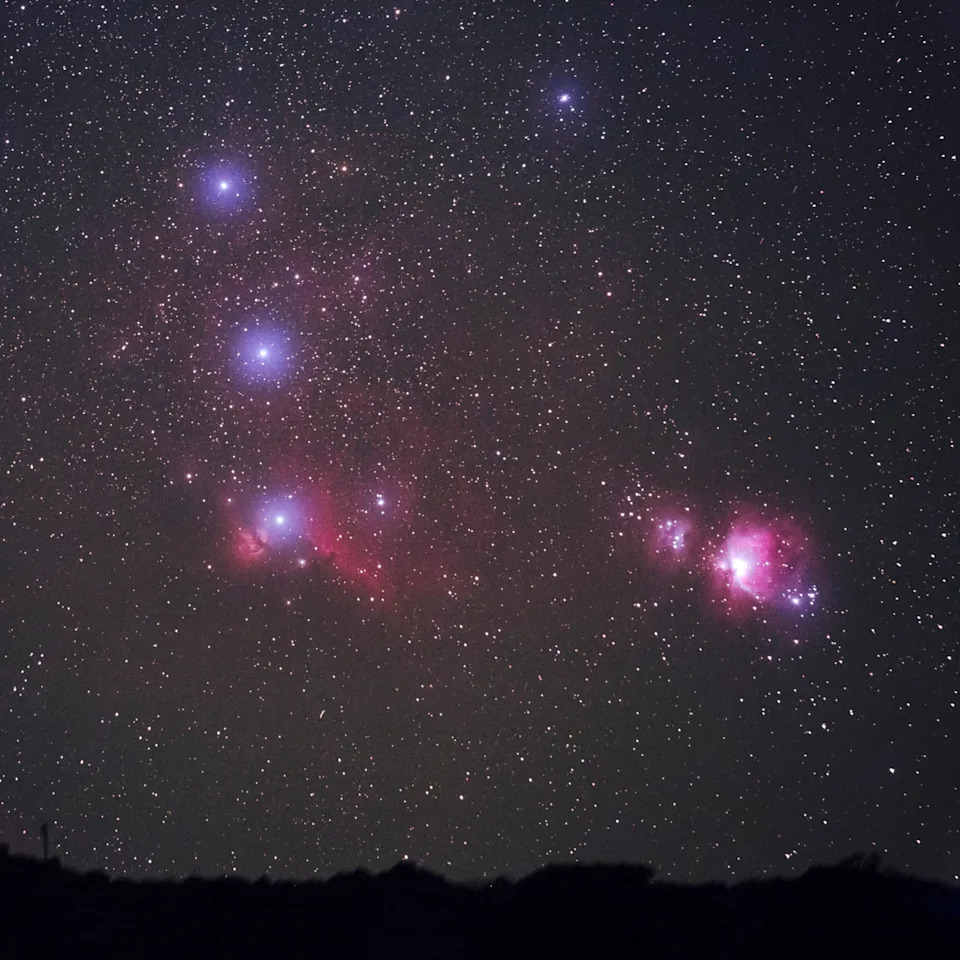 The pink and purple haze of Orion Nebula glowing amongst the bright stars of Orion's Belt