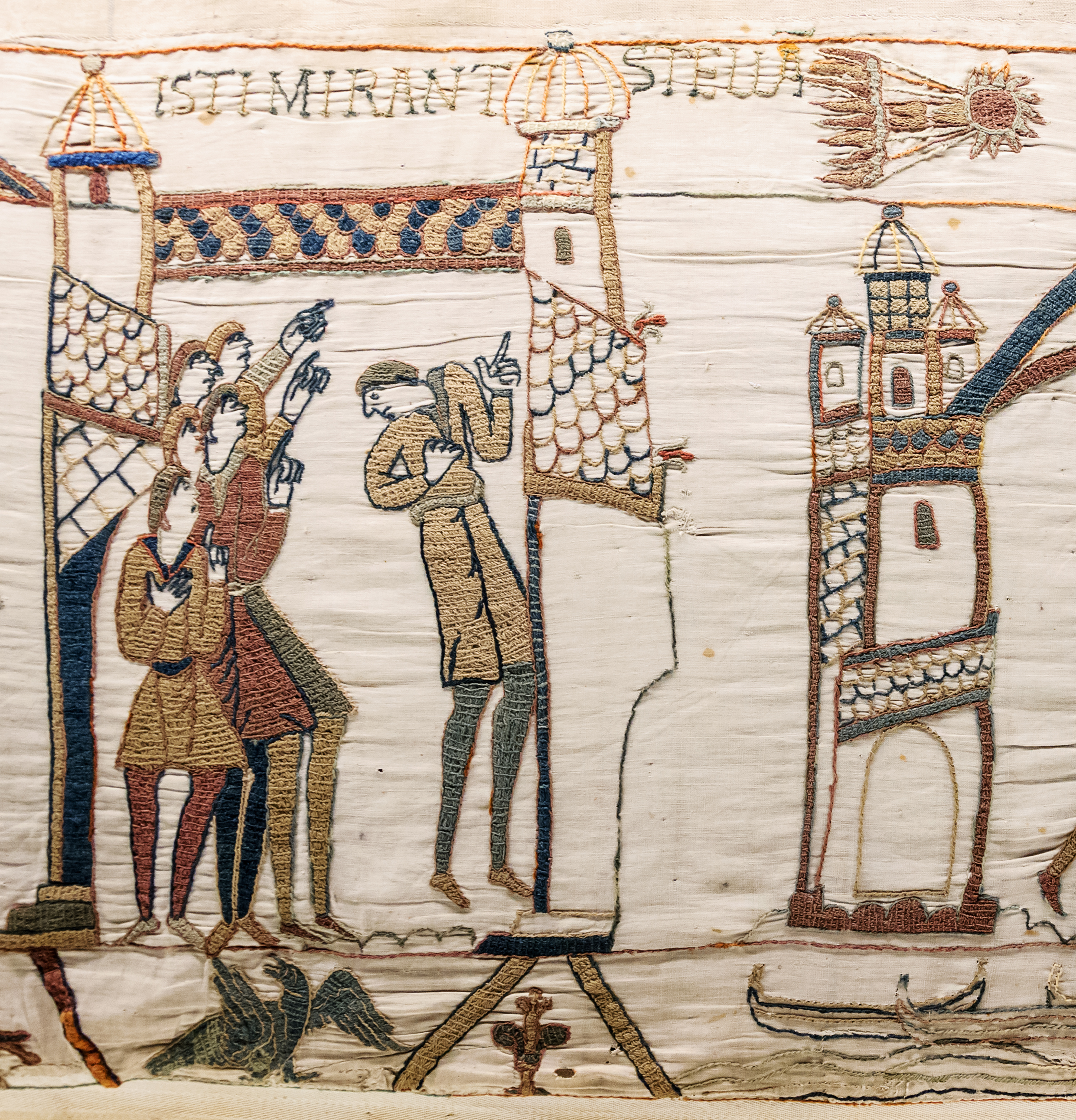 A portion of the tapestry showing a saw representaiton of the comet and sxi people inside a town point at the star.