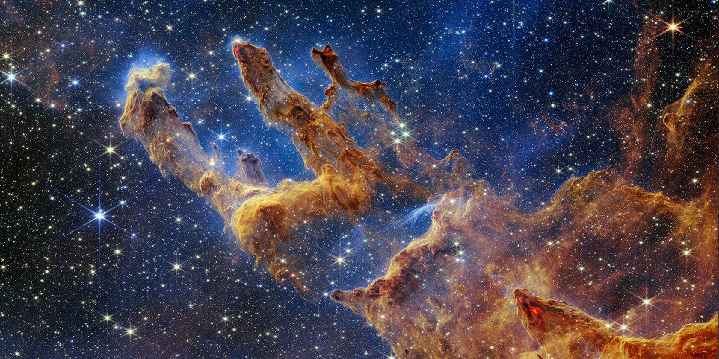 This cropped horizontal image has layers of semi-opaque rusty red colored gas and dust that starts at the bottom right and goes toward the top left. There are three prominent pillars rising toward the top left. The left pillar is the largest and widest. The peaks of the second and third pillars are set off in darker shades of brown and have red outlines.