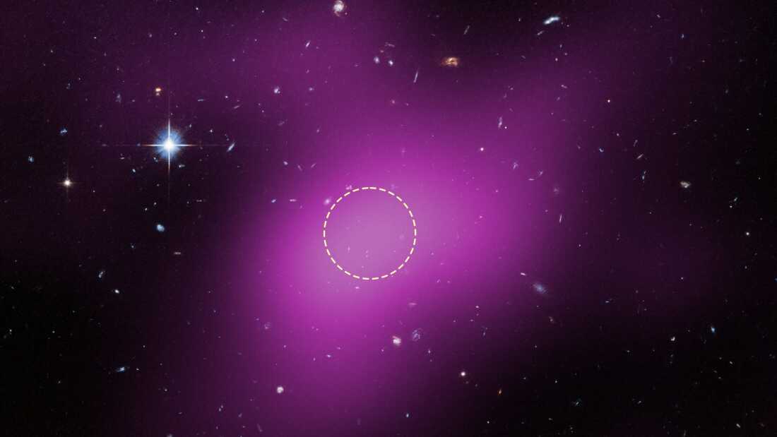 A black and purple background with bright white stars. A yellow circle in the middle of the image highlights a starless region, Cloud-9. 