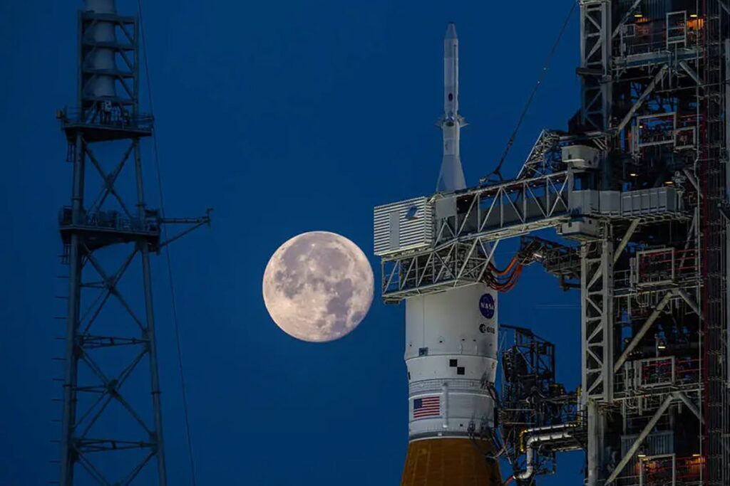 A full Moon behind the Artemis I Space Launch System rocket on the launchpad at NASA