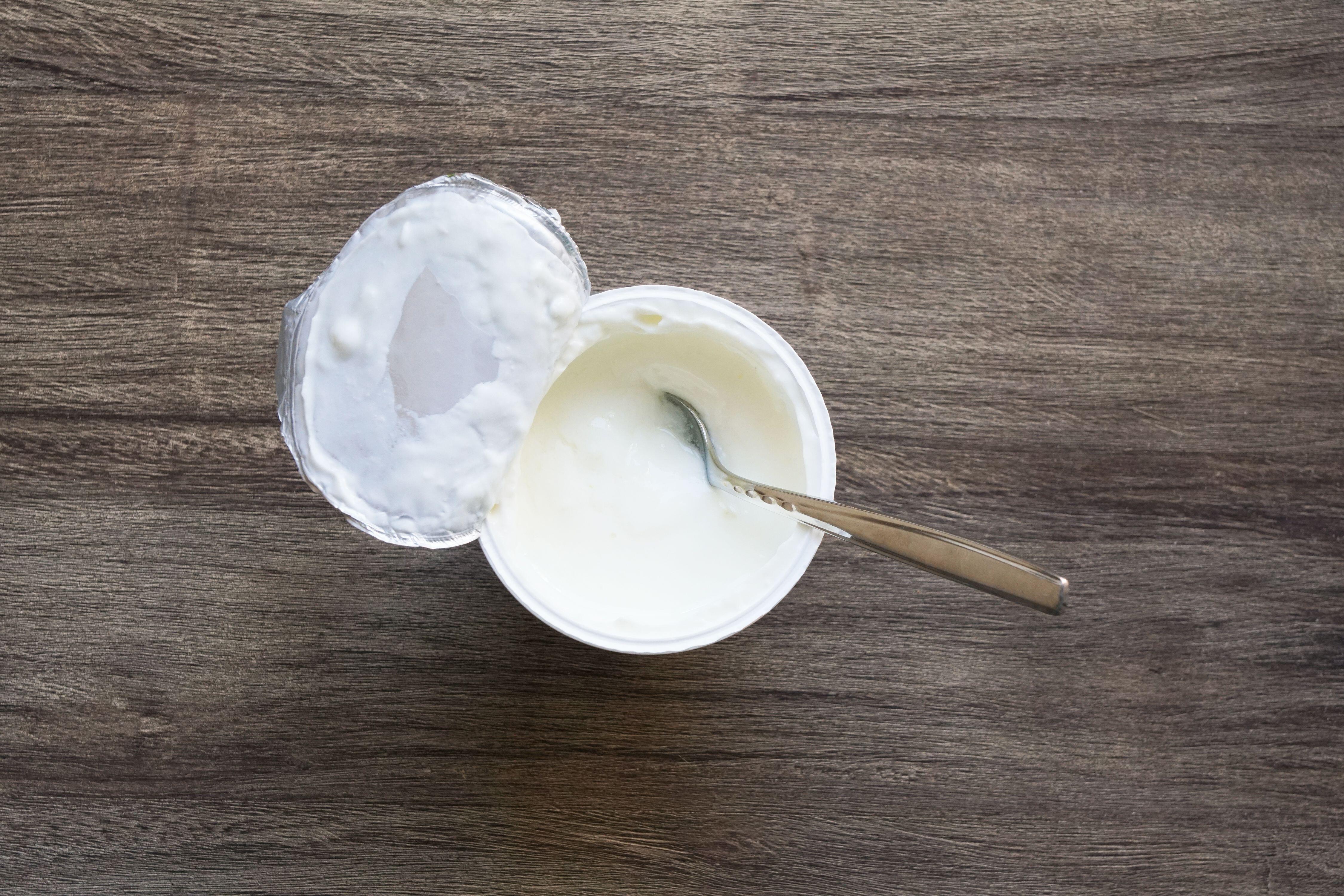 Overhead view of plain or natural yoghurt in yoghurt pot with dessert spoon