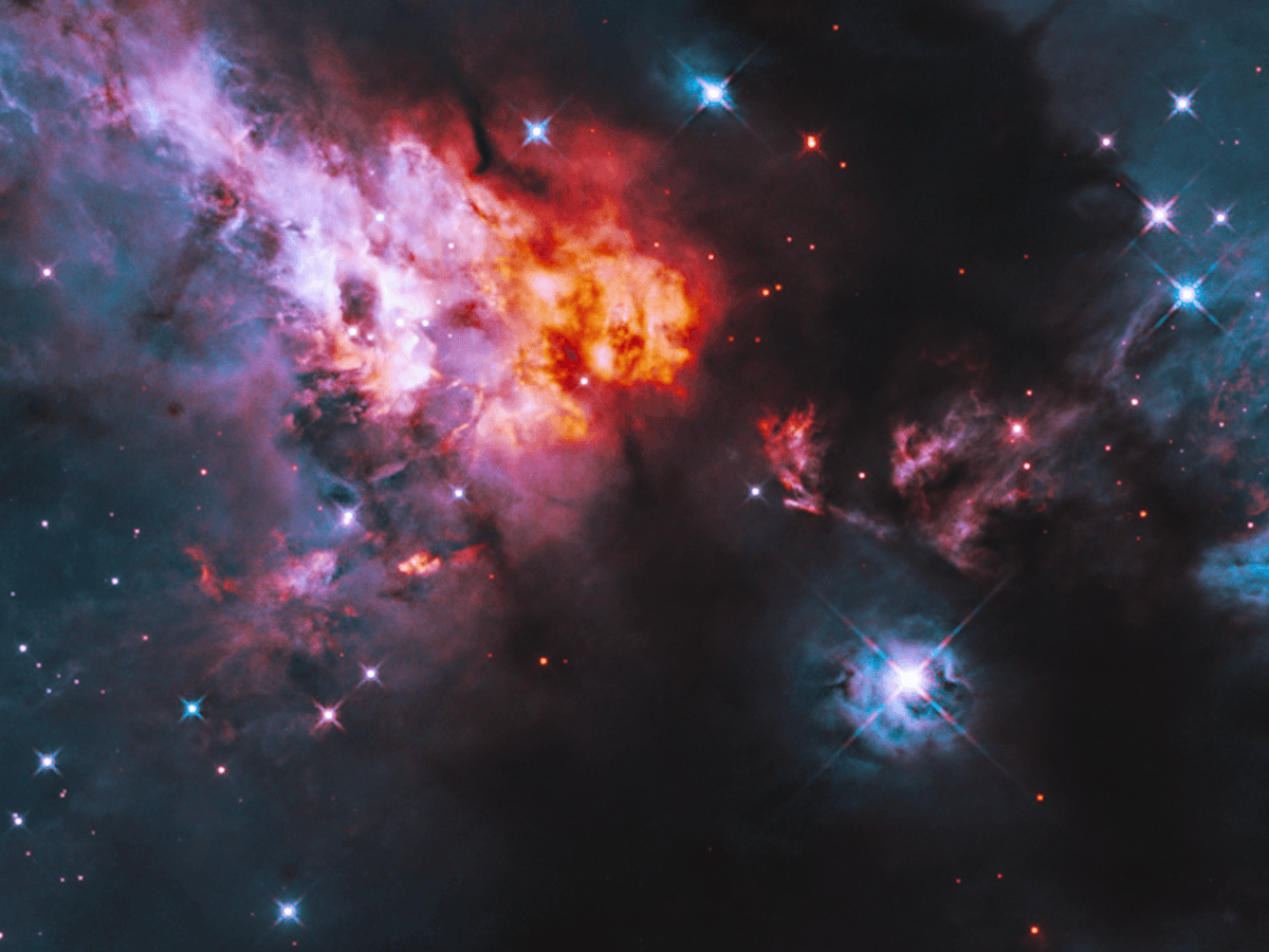 The Cepheus A region which is a region in space of orange, pink and blue stars against a dark space background. 