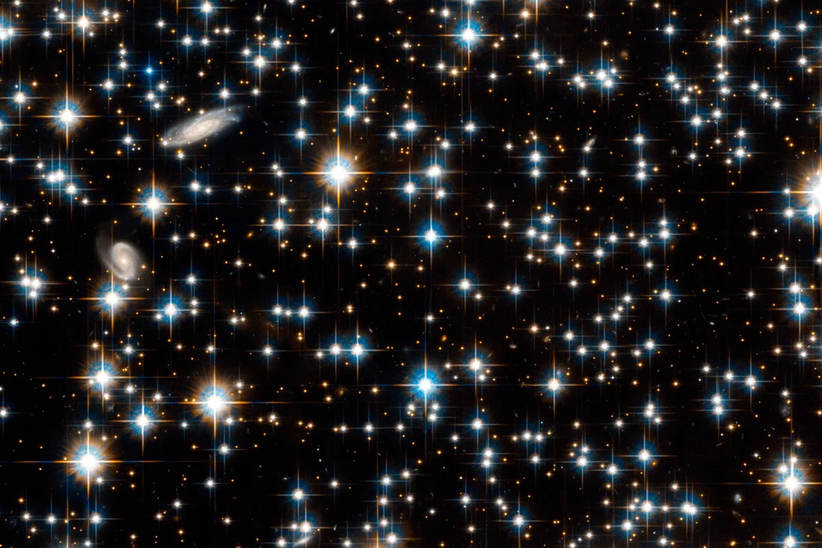 Open star cluster NGC 6791, Hubble Space Telescope image. The stars seen here are estimated to be 8 billion years old. Two background galaxies can be seen at upper left. The foreground stars cover an area around 10 light years across. NGC 6791 is some 13,300 light years from Earth, in the constellation of Lyra. Image data obtained in 2003 and 2005 with the Advanced Camera for Surveys instrument.