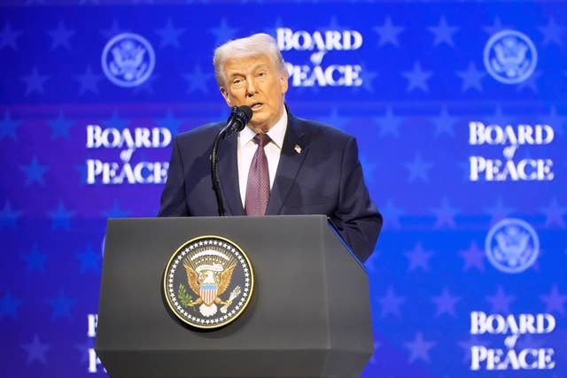 Donald Trump speaking behind a lectern in front of a blue backdrop featuring the words 'Board of Peace'