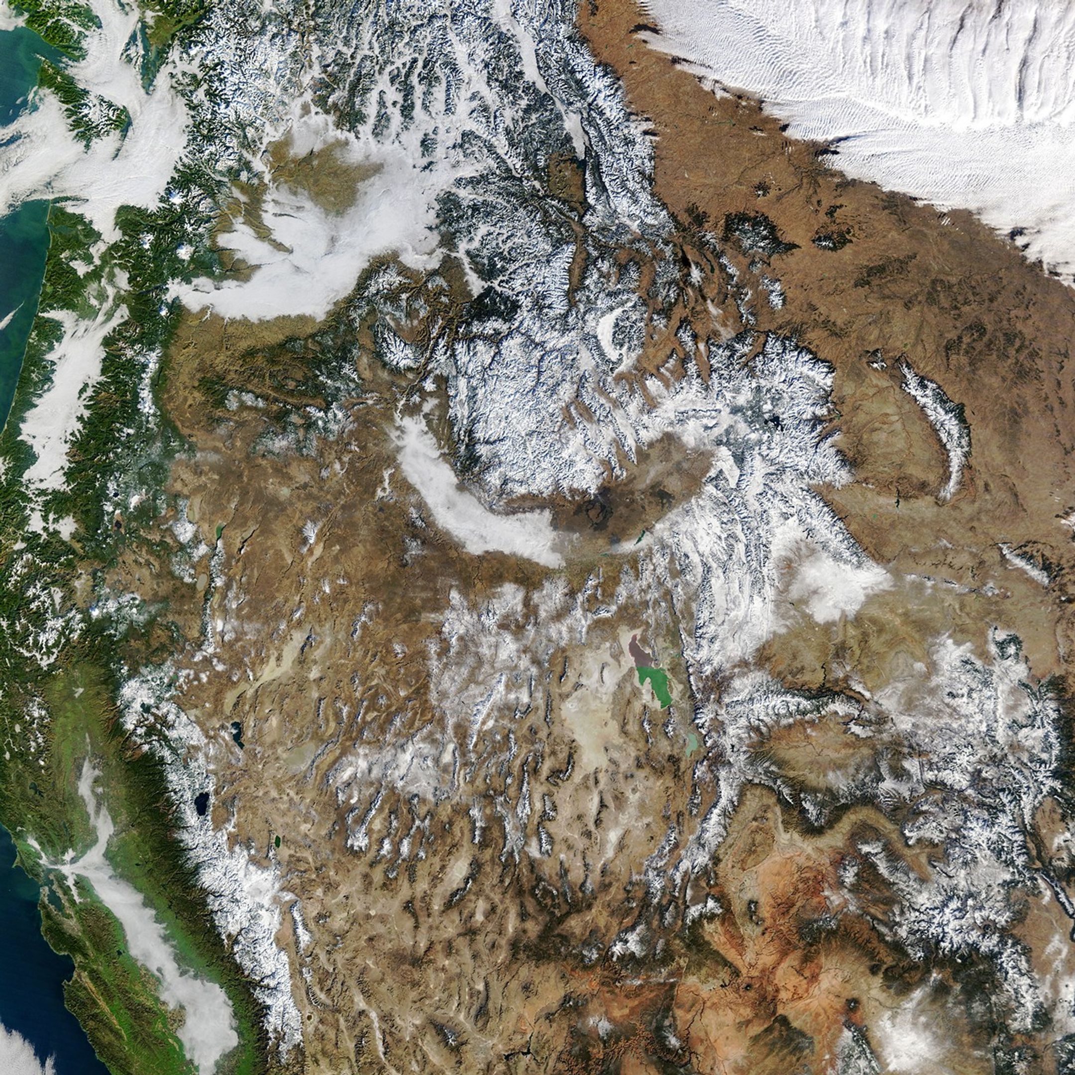 Snow covers some of the high-elevation areas across the western U.S. Areas of clouds and valley fog fill parts of the scene.