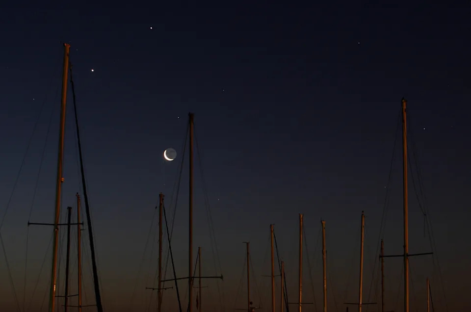 Stan Honda/AFP via Getty Images - PHOTO: In a rare alignment, the crecent Moon rises with the planets Venus (L) and Jupiter (top) over boat masts at a dock at dawn on February 4, 2008 in Titusville, Florida.