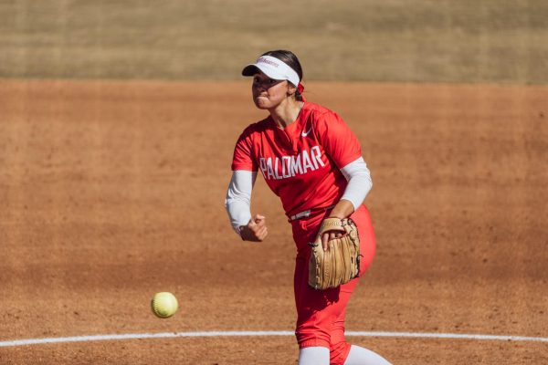Palomar softball pitcher Kiara Flaviani in a red uniform and white cap throws a pitch against the opposing batter, not pictured.