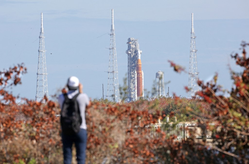 A person viewing the Artemis II Space Launch System rocket and Orion spacecraft on Launch Pad 39B in the distance.