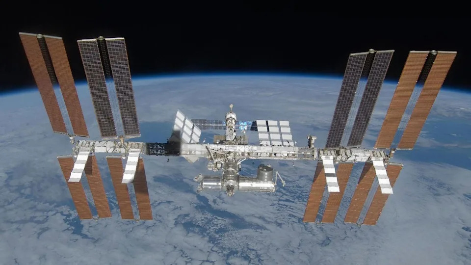An image of the International Space Station, with its many solar panels and modules, floating above Earth in space.