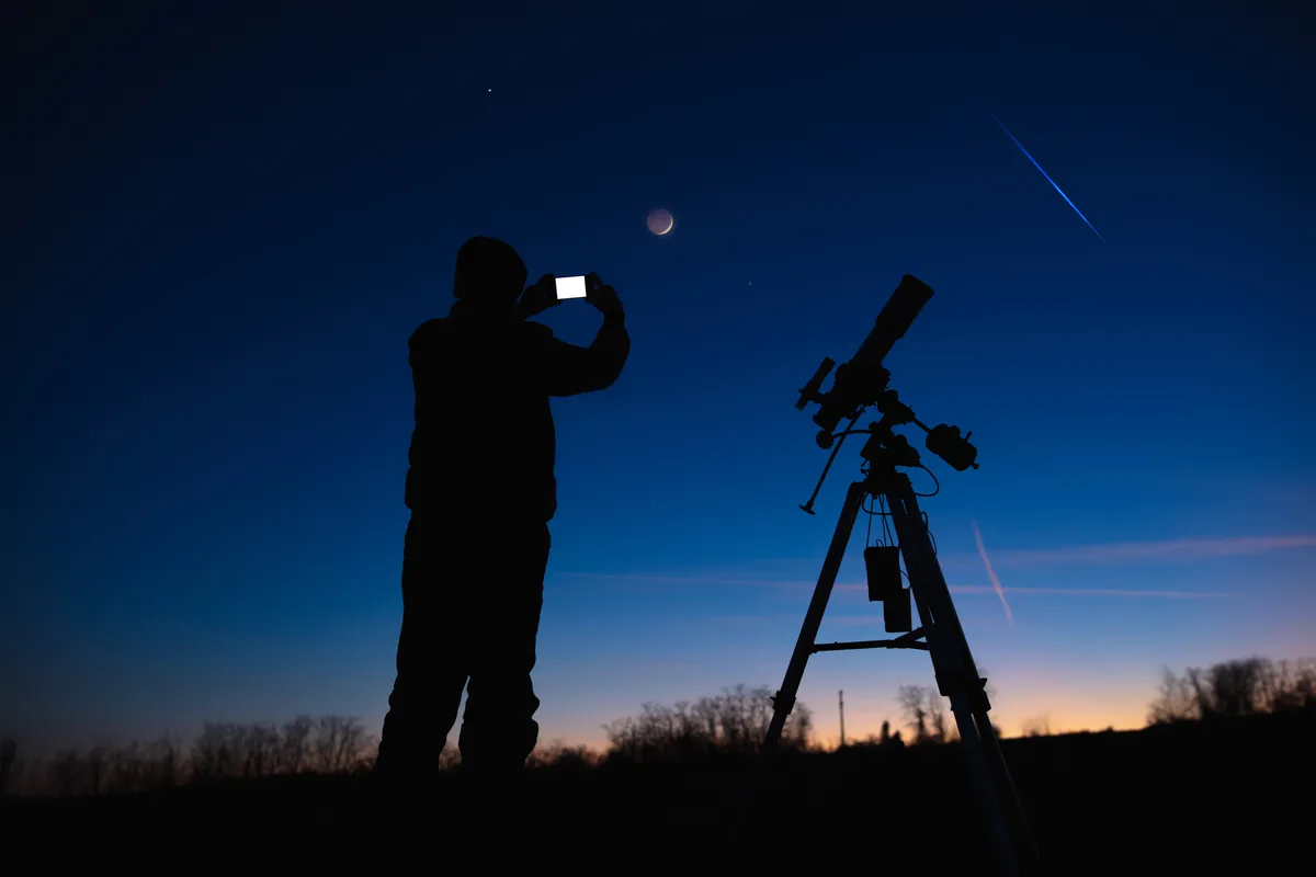 Silhouette of person photographing the Moon with their smartphone