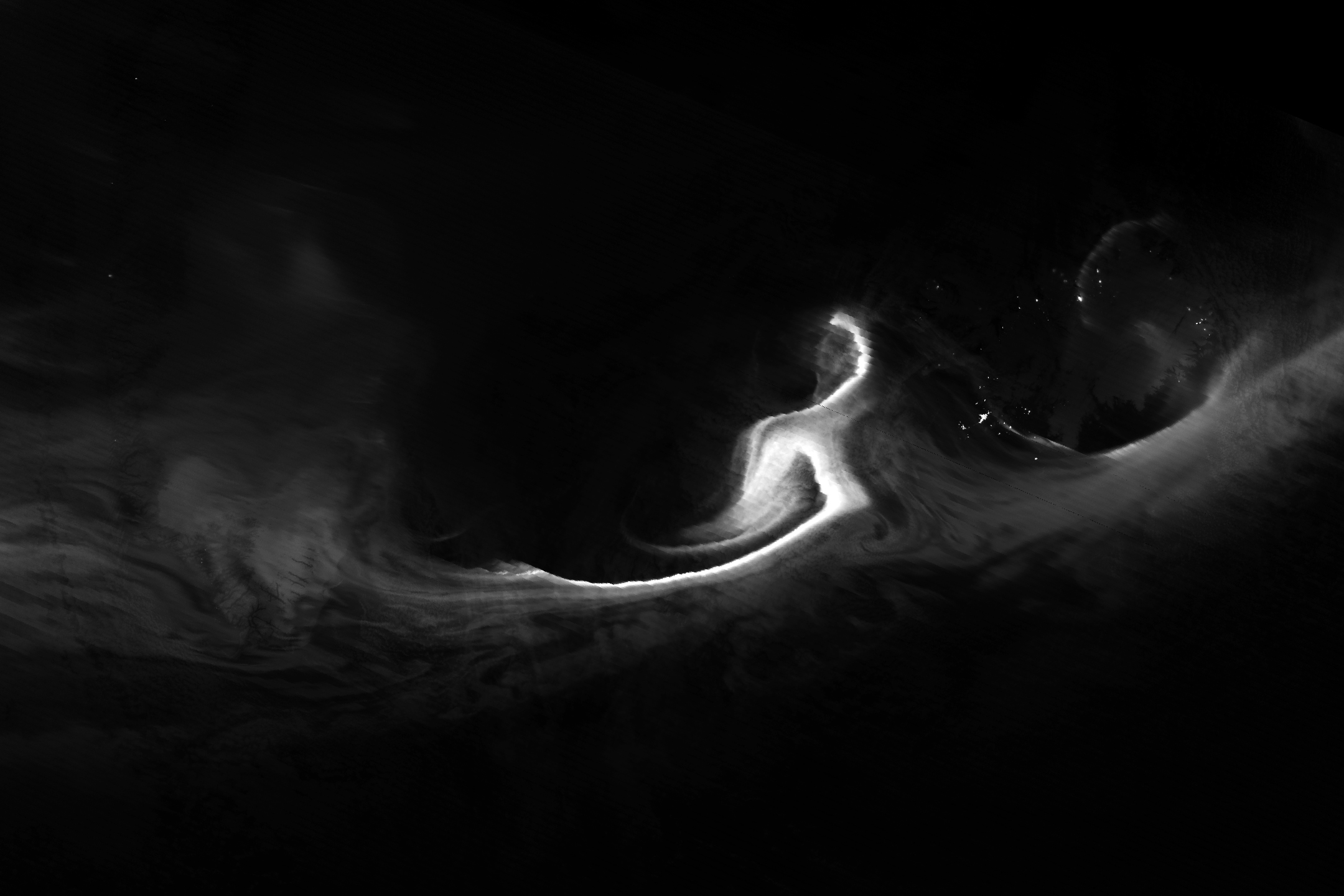 grayscale image showing bright sweeping structures - auroras, shining bright over specks of city lights below.