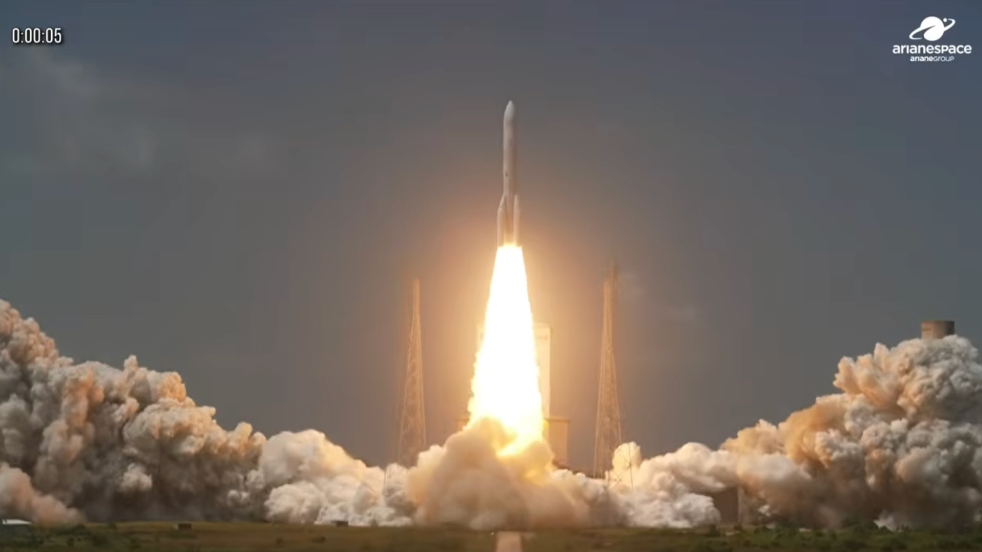 long-distance photo of a white rocket launching into a blue sky, with a huge plume of exhaust billowing around it