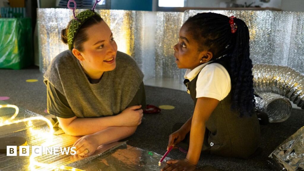 Two girls in blue uniforms are focused on etching designs into metal plates