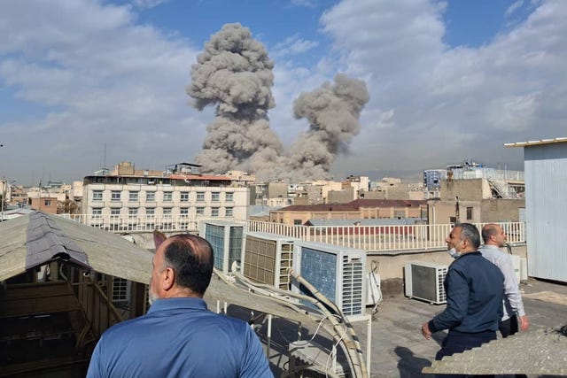 People watch as smoke rises on the skyline after an explosion in Tehran