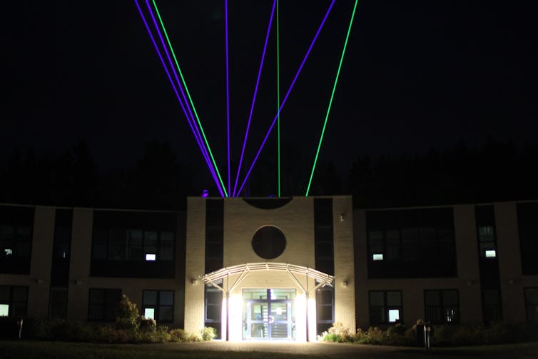 Blue and green lasers shining out of the roof of a large building.