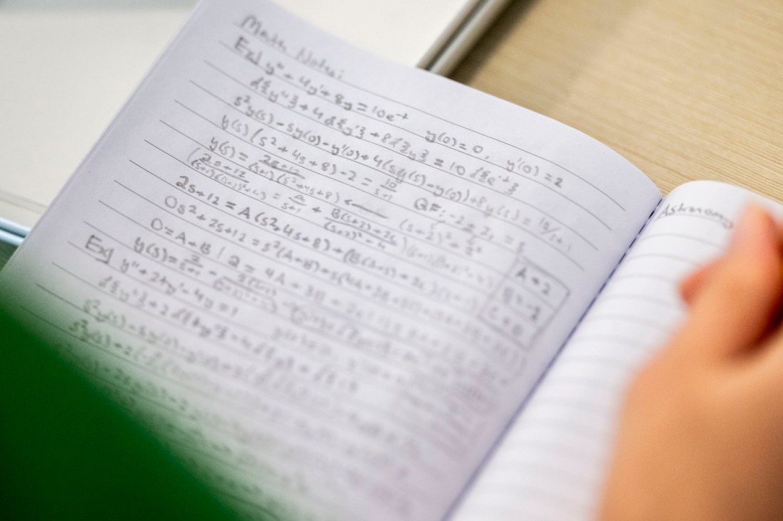 A close up of a handwritten notebook filled with equations and scientific notes, held open by a person's hand. 