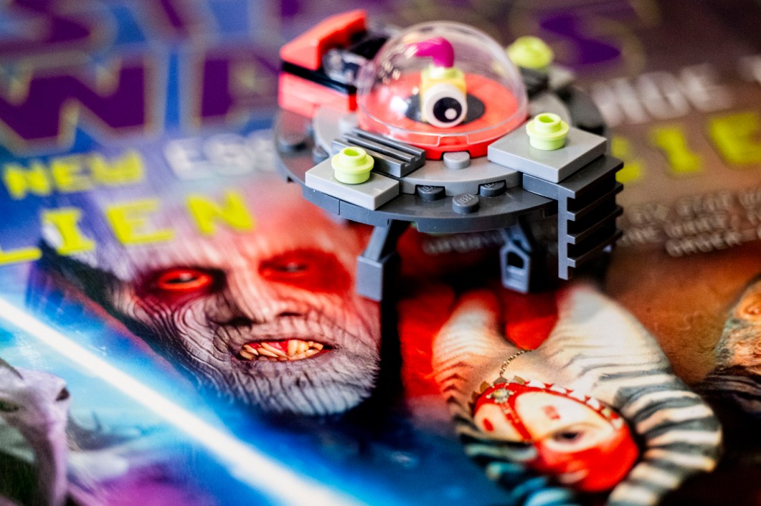 A LEGO spaceship model sits on top of a colorful science fiction book cover featuring an alien illustration.
