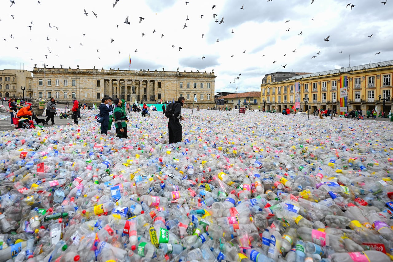 People walk through a large plaza covered in empty plastic bottles 