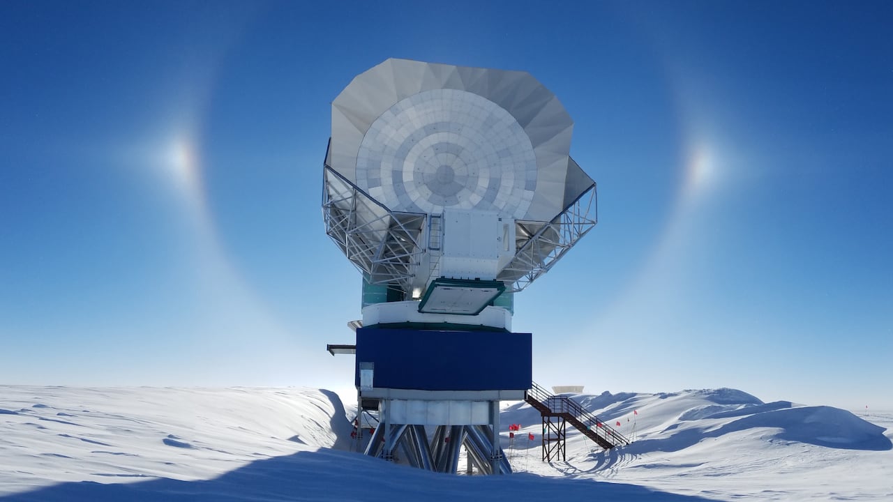 A metallic structure with a large satellite dish stands in a snowy ground against a blue sky. 