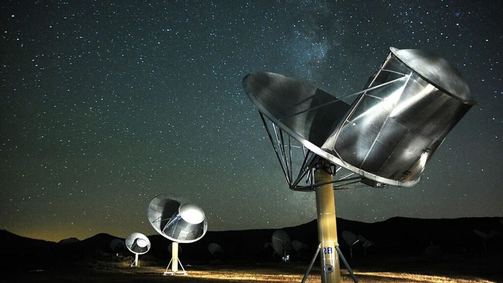 three silver radio telescopes stand beneath a starry night sky