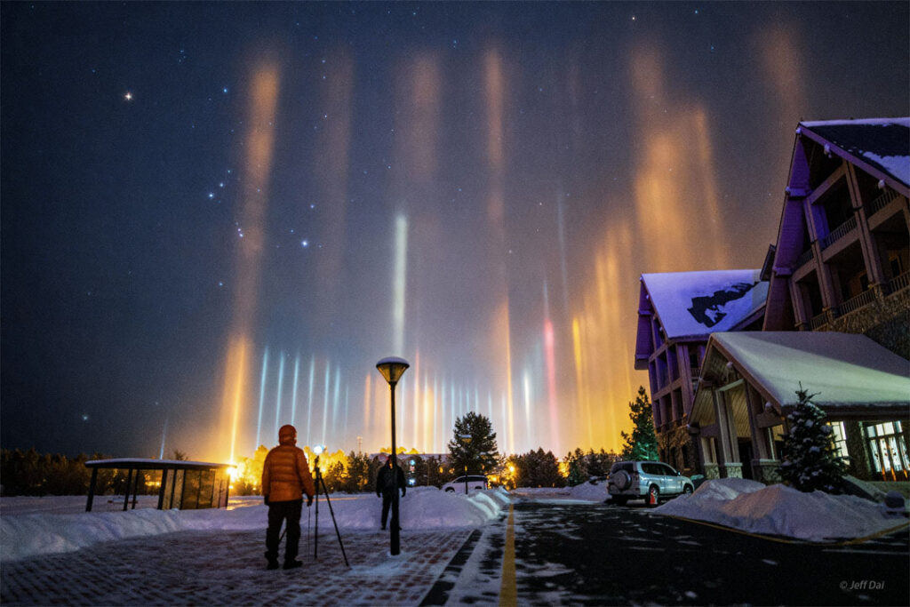 2026 March 23 – Light Pillars and Orion over Mohe A starry sky appears above a snowy street with a
house on the right. The constellation of Orion is
visible on the left. Up from the ground many pillars
of light are seen. Two people stand watching the pillars
on the street in the foreground.
Please see the explanation for more detailed information.