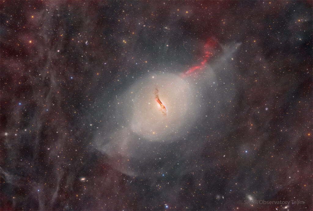 2026 March 30 – Peculiar Elliptical Galaxy Centaurus A A starfield glows faintly with red glowing gas and dust.
In the center there is some sort of unusual galaxy with a red jet
emanating toward the upper right and a dark dust lane through
its center.
Please see the explanation for more detailed information.