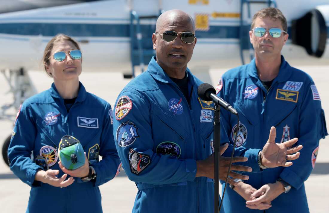 Artemis II crew members — mission specialist Christina Koch (left) and commander Reid Wiseman (right) — listen as pilot Victor Glover speaks to the media after arriving at the Kennedy Space Center on March 27, 2026 in Cape Canaveral, Florida. The astronauts' planned 10-day mission will take them around the Moon and back to Earth.