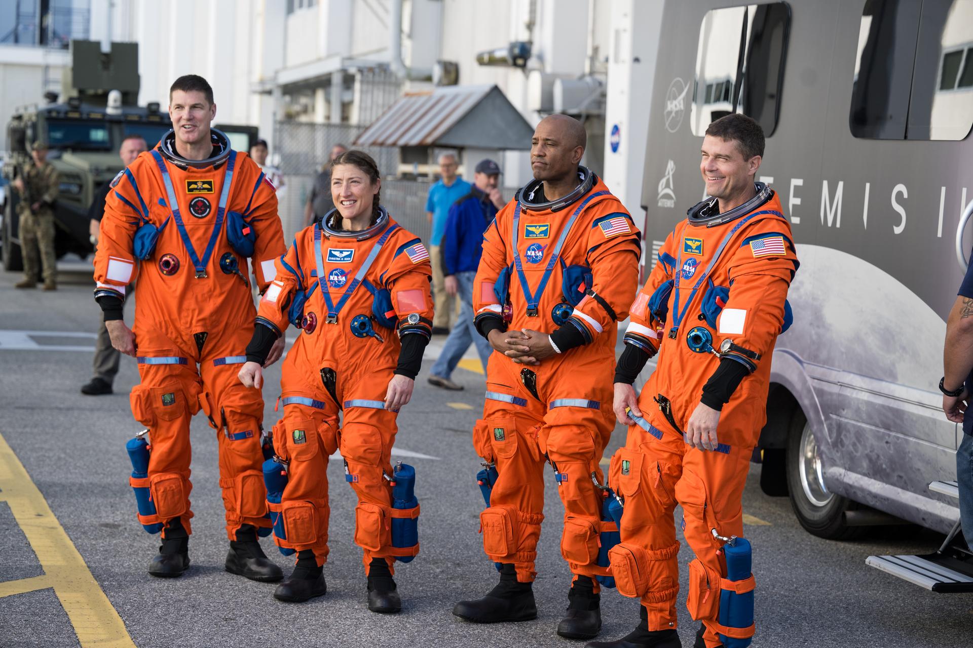 Four people in orange spacesuits stand on a road