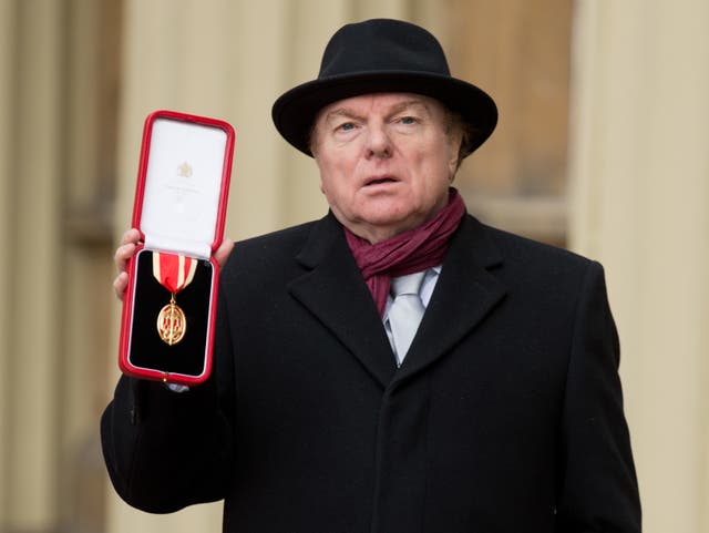Van Morrison holding his medal at Buckingham Palace